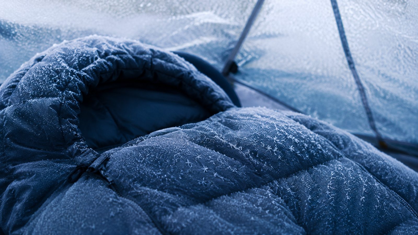 Frostkristaller på huvan av en sovsäck i kallt blått morgonljus inne i ett tält